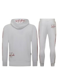Witte hoodie en jogger set in een gladde stof. Rode accenten op de mouwen en joggers. Capuchon met stikseldetails. Merkbewerking op de borst en dij.