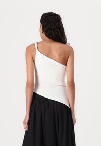 Top alb asimetric cu o curea răsucită, corset ajustat și margine fluidă, asociat cu o fustă neagră. Textură netedă, design minimalist.