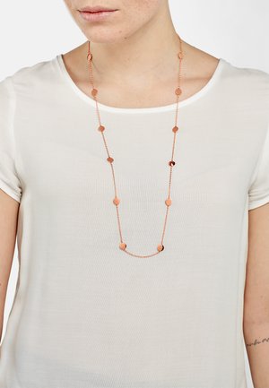 Lange roségouden ketting met ronde en ovale schakels, textuurketting, gedragen over een witte top. Eenvoudig ontwerp, lichtgewicht materiaal.