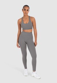 Gray athletic crop top and high-waisted leggings made of stretchy fabric. Features a smooth texture and minimalistic design. White sneakers.