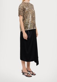 Zlatý a černý top s flitry a leopardím potiskem, spárovaný s černou sukní. Sandály mají střih s pásky a nízký blokový podpatek.