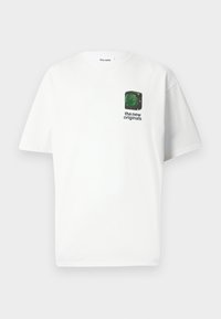 Hvit bomulls T-skjorte med korte ermer. Har et lite grønt grafisk motiv og tekst i svart på venstre brystområde. Klassisk T-skjortedesign med rund hals.