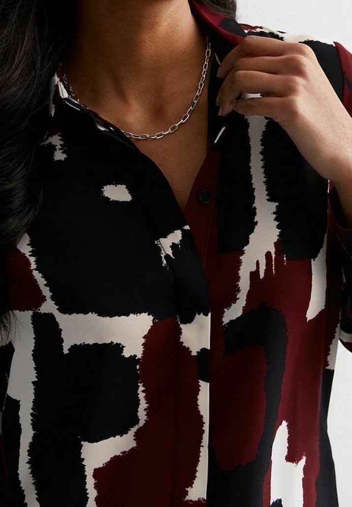 Camicia button-up nera, borgogna e crema. Presenta un motivo astratto con una vestibilità rilassata, colletto e maniche corte. Collana con catena metallica.