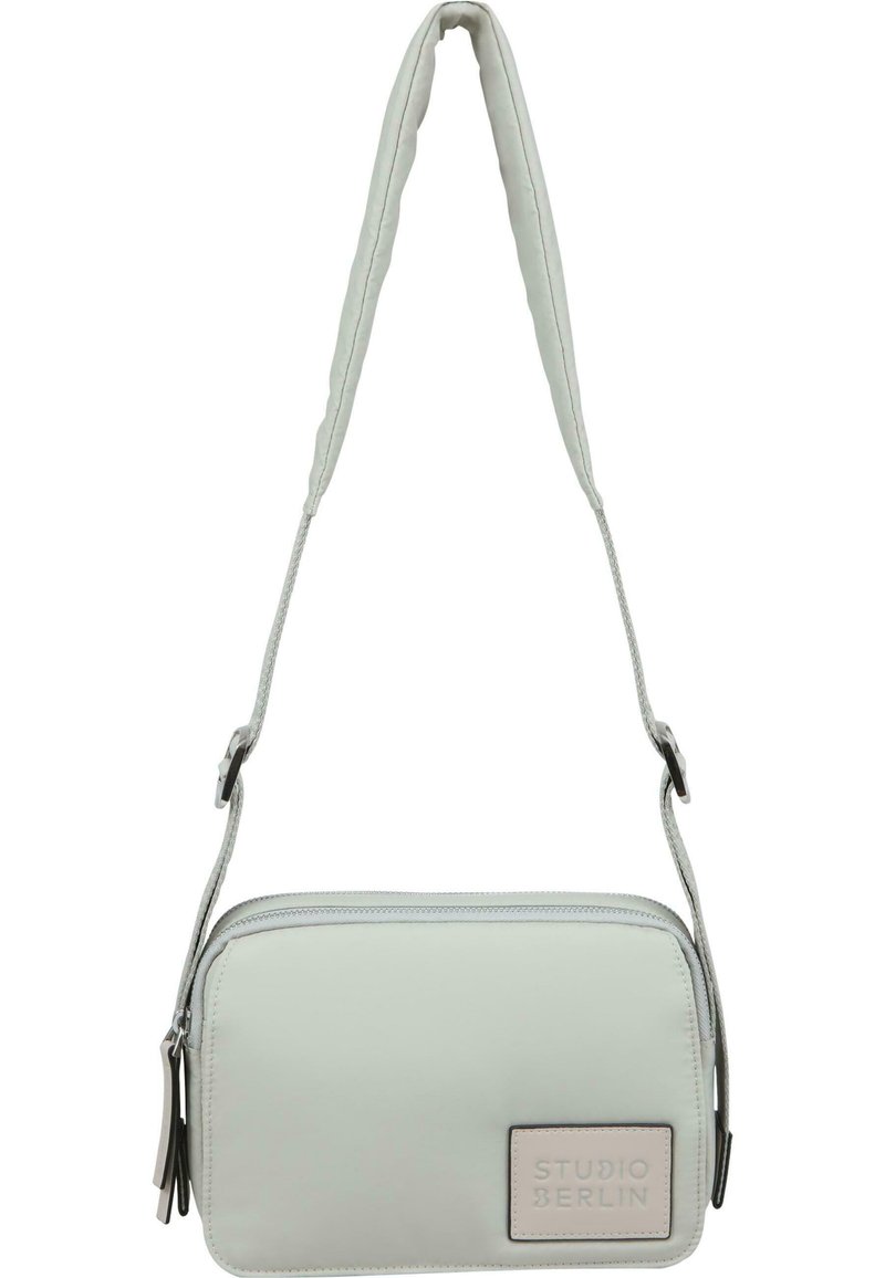 Lys grå crossbody-veske laget av glatt materiale, med rektangulær form, justerbar stropp og preget "STUDIO BERLIN"-logo.