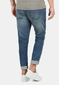 Denimske hlače v srednje modri barvi z blagim zbledelostjo, slim fit kroja in zavihanimi manšetami. V kombinaciji z belimi športnimi copati. Nalepka na zadnjem žepu.