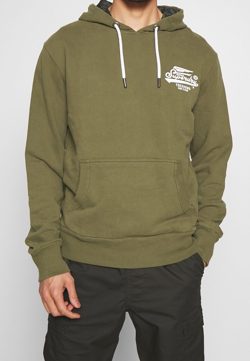 Felpa con cappuccio verde oliva in tessuto morbido, con tasca a marsupio frontale, coulisse e stampa del logo bianco sul petto.