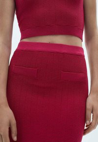 Red ribbed knit top paired with a matching midi skirt. Skirt features two textured patch pockets and a smooth waistband.