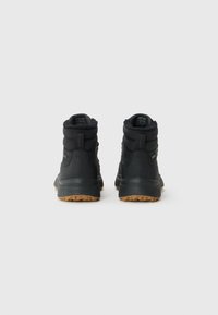 Pair of black winter boots with fur lining and brown rubber soles, shown from the back on a white background.