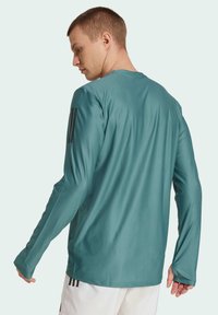 Langärmliges Sportshirt in Teal, mit strukturiertem Stoff, runder Ausschnitt und schwarzen Streifen an den Ärmeln zur Akzentuierung.