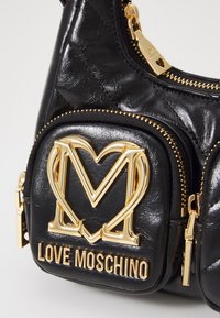 Černá texturovaná kožená kabelka Love Moschino se zlatým srdcovým logem M a zlatými zipy na přední kapse a hlavním prostoru.