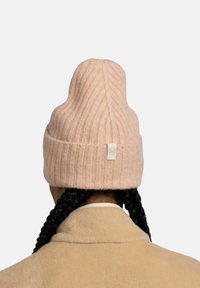 Light pink ribbed beanie with a peak top and a small tag at the back. The texture is soft, and it is worn with a beige coat.