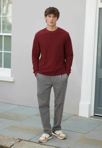 Maron farvet langærmet skjorte, grå plisserede bukser og multicolore sneakers. Glat stof, afslappet pasform og lagdelte designdetaljer.