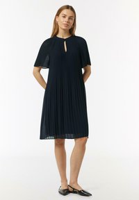 Navy-gefülltes Kleid mit einem Schlüssellochausschnitt und kurzen, flatternden Ärmeln. Leichter Stoff mit glatter Textur, fällt über die Knie.