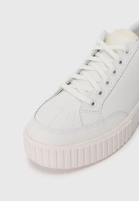 Sneaker en cuir blanc avec une semelle en caoutchouc texturée. Présente un bout arrondi, des accents cousus et des lacets plats. Conçu dans un style minimaliste.