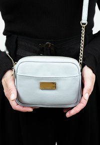 Lichtblauwe neplederen schoudertas met een goudkleurige hardwareplaat, rechthoekige vorm, ritssluiting en een kettingband.