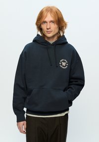 Navy sweatshirt with a hood, front pocket, and circular logo. Made from soft fabric, featuring a relaxed fit and ribbed cuffs.