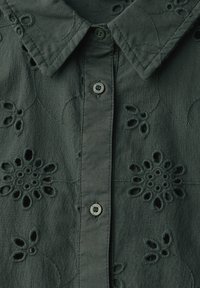 Donkergroen shirt met geborduurde bloemenpatronen, een klassieke kraag en knoopsluiting met bijpassende knopen. De stof voelt licht aan.