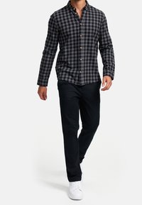 Czarna i szara koszula w kratę na guziki z długimi rękawami, zestawiona z czarnymi spodniami i białymi trampkami. Koszula ma drewniane guziki i kołnierzyk.