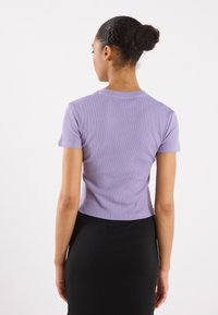Purple ribbed cropped t-shirt with short sleeves, round neckline, and a fitted shape, paired with a black form-fitting skirt.