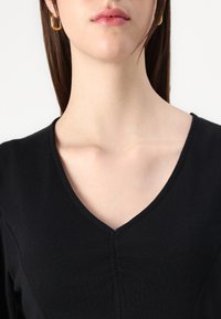 Sort V-hals top med en struktureret design, glat tekstur og diskret stiksyning langs midten.