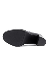 Scarpa nera con tacco alto, dotata di una suola in gomma testurizzata, con un design elegante e una punta affilata, realizzata in morbida pelle.