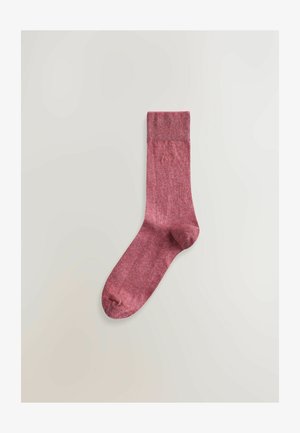 Bordo krāsas zeķe, izgatavota no strukturētas adījuma materiāla, ar ribotu aproci un nelielu austu logotipu pie augšas.