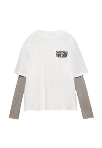 Hvid T-shirt med korte ærmer lagdelt over en grå langærmet skjorte. Har fed sort tekst: "DANCE FIRST THINK LATER" på brystet.