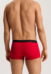 Boxer da uomo rossi con una vita nera che mostra il nome del marchio, caratterizzati da un tessuto liscio e una vestibilità aderente.
