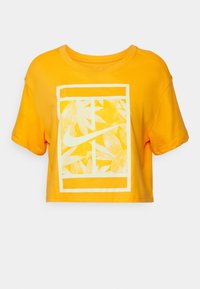Cropped yellow t-shirt made of cotton, featuring a white rectangular graphic with a leaf pattern and a Nike logo in the center.