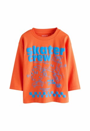 Narancssárga hosszú ujjú póló kék "skater crew" felirattal, és egy rajzfilmszerű keksz és tejkarton, amint gördeszkáznak.