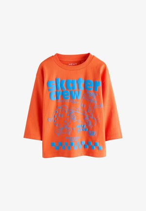 Oranžové tričko s dlhým rukávom s modrým textom „skater crew“ a kresleným sušienkou a kartónom mlieka na skateboardoch.