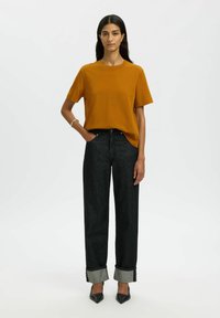 Sinapse dzeltena īsām piedurknēm T-krekls, apvienots ar tumšiem, plašiem džinsiem ar uzlocītām malām un melniem augstiem papēžiem.