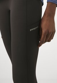 Black leggings made of stretchy, smooth fabric featuring a side pocket and discreet logo placement, with flat seams for a streamlined look.