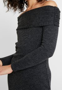 Robe à manches longues, décolletée sur les épaules, en tissu tricoté côtelé gris foncé, présentant une coupe ajustée avec une texture subtile et des accents froncés.