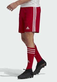 Red soccer shorts with three white stripes on the sides, paired with red socks featuring white stripes and black cleats with gold accents.