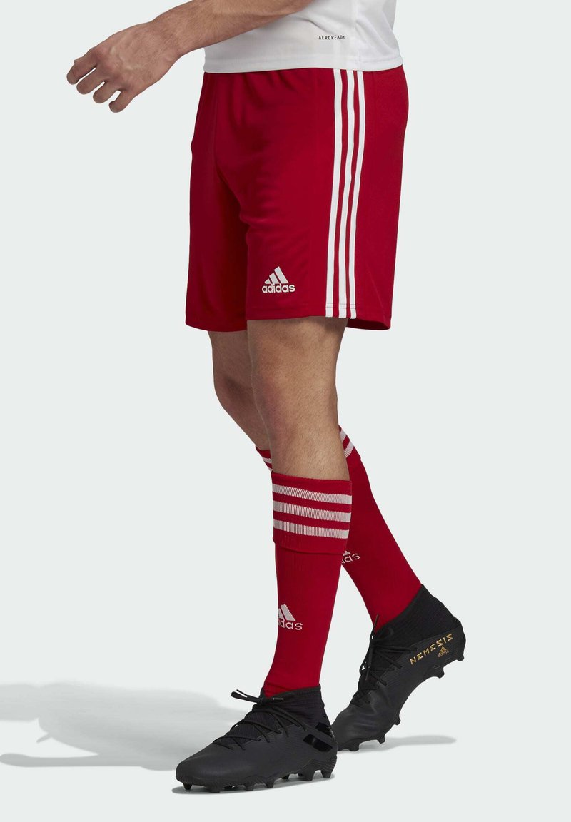 Red soccer shorts with three white stripes on the sides, paired with red socks featuring white stripes and black cleats with gold accents.