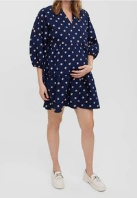 Navy-muotoinen mekko kukkakuviolla, V-pääntiellä ja pallohihnoilla. A-linjainen malli, jossa on kerrokselliset röyhelöt, täydentäen rentoa istuvuutta mukavuutta varten.