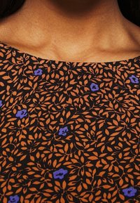 Svart tyg med ett orange och blått blommönster. Designen har spridda blad och små blommor, med en slät textur.