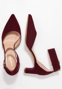 Burgundy mockasins med blockklack, spetsiga tår, ankelrem och detaljer i guldton. Slät innersula och platt yttersula.