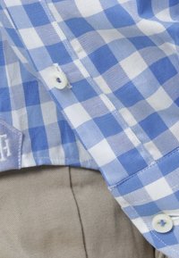 Niebieska i biała koszula w kratkę z białym guzikiem oparta na beżowej tkaninie spodni.