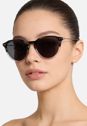 Occhiali da sole rotondi neri con finitura opaca, dettagli in metallo e lenti scure. La montatura ha un bordo trasparente che aggiunge un tocco di design distintivo.