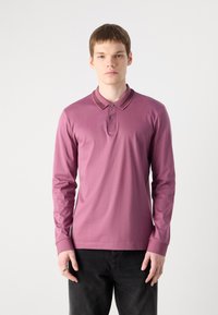 Camisa polo de manga longa em mauve, com colarinho clássico, pala com botões e punhos em ribana, combinada com jeans escuros.