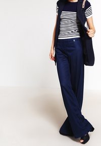 Pantalones de pierna ancha de color navy con una textura suave, combinados con una blusa de rayas de manga corta. Un chaleco ajustado completa el conjunto.