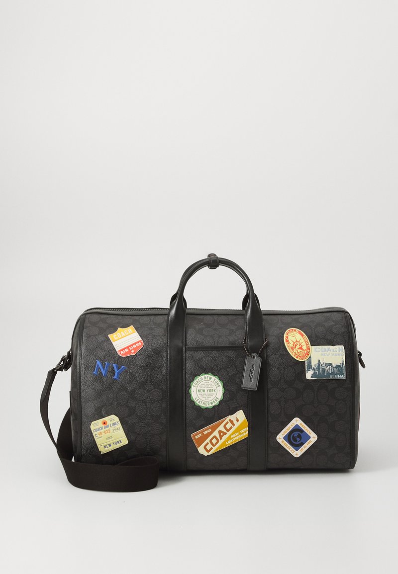 Zwarte leren reistas met stofaccenten, voorzien van verschillende reizigersstickers, dubbele handgrepen en een verstelbare schouderband.