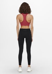 Reggiseno sportivo rosso con design a racerback abbinato a leggings neri con tessuto aderente e liscio e sottili dettagli cuciti.
