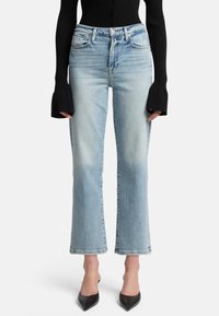Jeans in denim azzurro chiaro con vita alta, taglio dritto e orlo grezzo. Abbinati a un top nero a coste con maniche lunghe e décolleté nere con punta.
