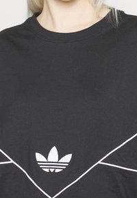 Black Adidas shirt with white trefoil logo centered below the neckline and white diagonal lines across the chest.