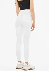 Vit skinny jeans med hög midja, två bakfickor och en slät textur. Kombinerat med en svart kort topp och vita sneakers.