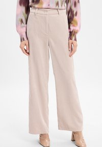 Beige wijde corduroy broek gecombineerd met nude glanzende leren blokhak enkellaarsjes en een bloemenroze trui.