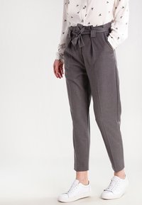 Szare dopasowane spodnie z wysokim stanem i paskiem do wiązania, z tapered nogawkami. Połączone z białą koszulą i białymi sneakersami.